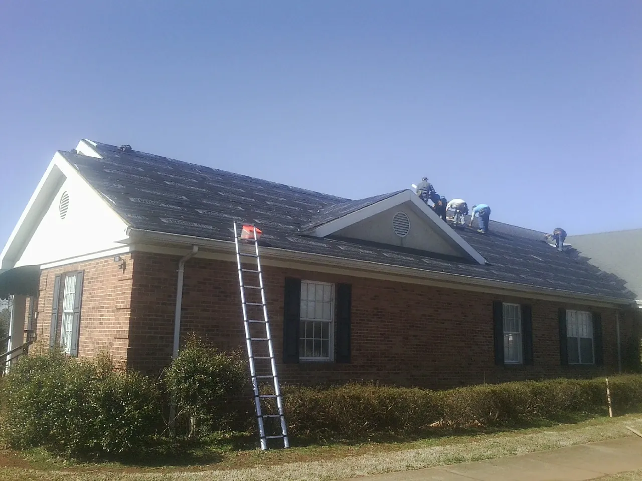Crew tearing shingles off a brick ranch roof with a ladder set — Metal Roof Repair work by our crew in Olivehurst