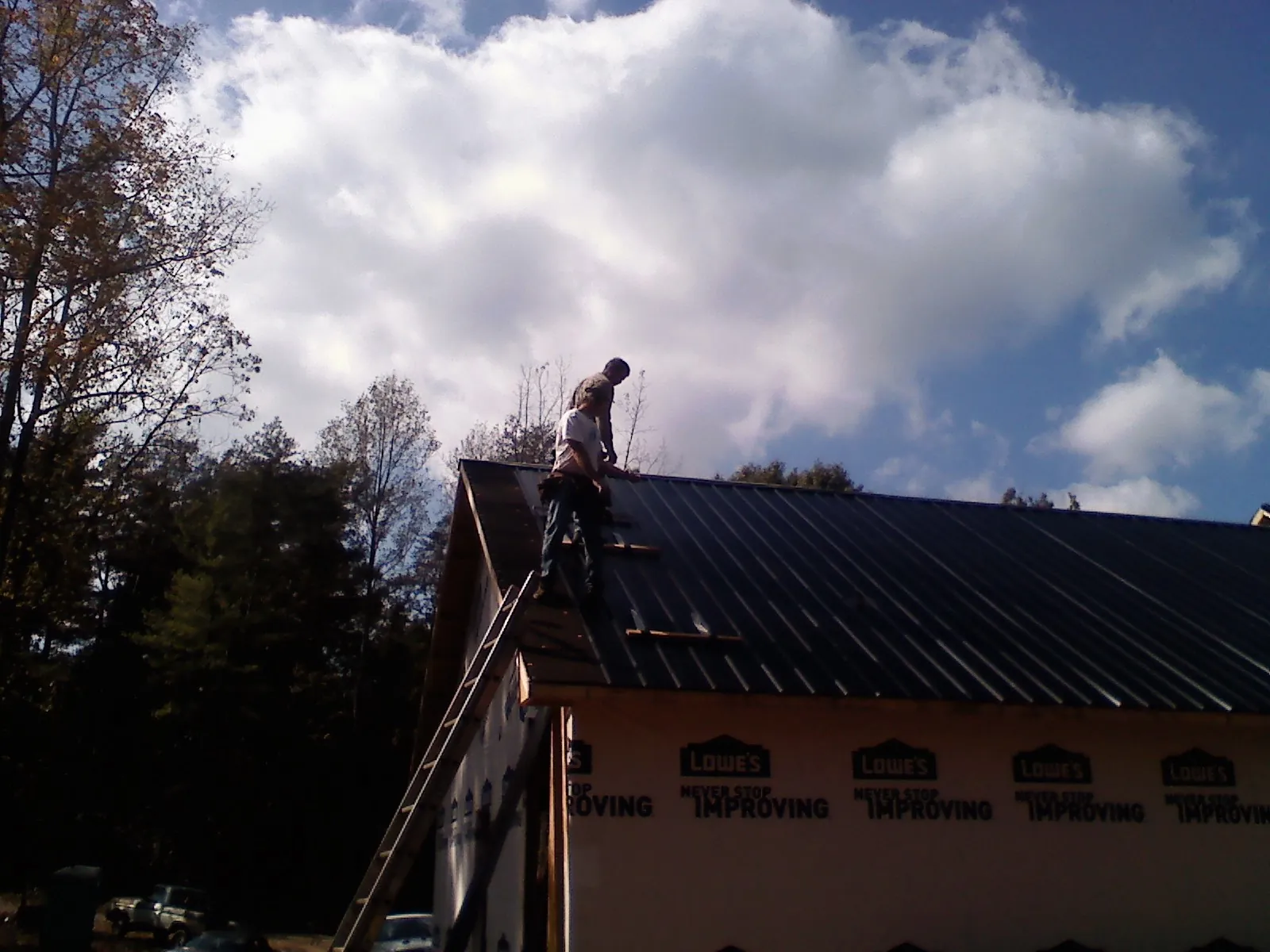 Roofer fastening dark metal panels high against a cloudy sky, from a Roof Inspection job in Olivehurst